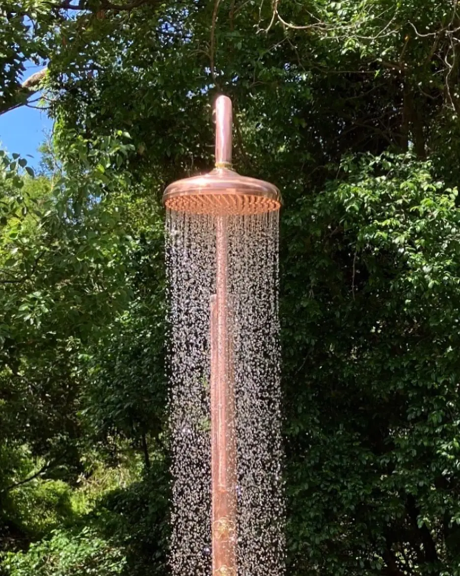 Tall copper outdoor shower backlit against trees