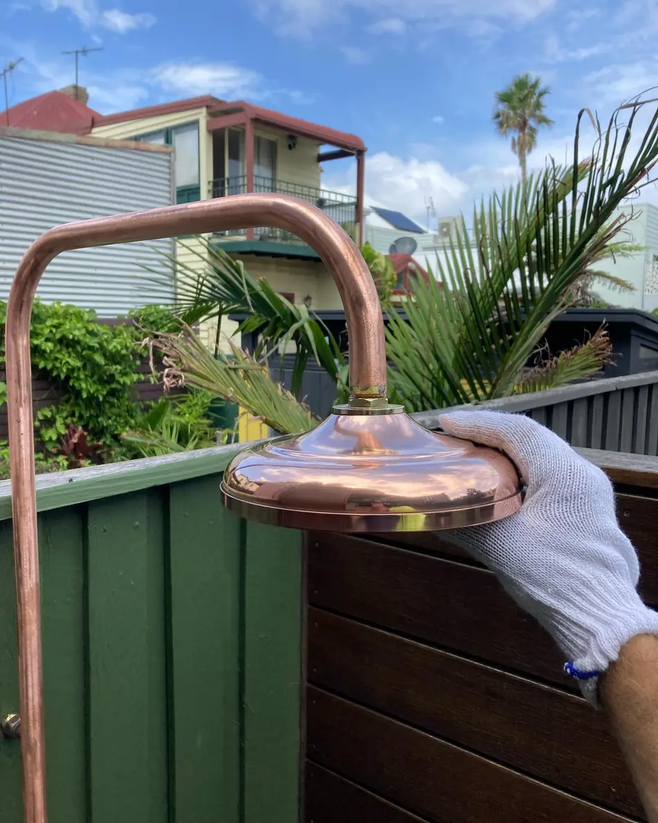 A hand holding a brass shower head fitting outdoors, before installation